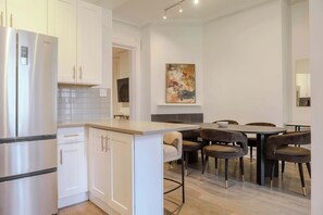 A modern kitchen with white cabinetry, a built-in island, and a dining area with dark chairs and a table. - Designer Loft 4E | Heart of Gold Coast/River North (Chicago)