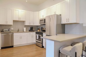 A modern kitchen with white cabinetry, stainless steel appliances, a built-in oven, and a microwave. - Designer Loft 4E | Heart of Gold Coast/River North (Chicago)