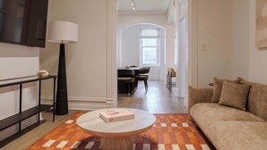 A modern living room with a sofa, a coffee table with a book, a lamp, and a television. - Designer Loft 4E | Heart of Gold Coast/River North (Chicago)