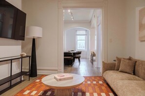 Ein modernes Wohnzimmer mit einer Couch, einem Couchtisch mit einem Buch, einer Lampe und einem Fernseher.