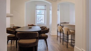 A dining area with a round table and multiple chairs, a window with blinds, and a view of buildings outside. - Designer Loft 4E | Heart of Gold Coast/River North (Chicago)