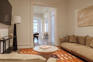 A living room with a sofa, a coffee table, and a TV. There is a dining area visible through an open doorway. - Designer Loft 4E | Heart of Gold Coast/River North (Chicago)