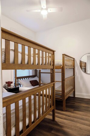 A room with two bunk beds, a ceiling fan, a bedside table with a lamp, and a mirror on the wall. - Designer Loft 4E | Heart of Gold Coast/River North (Chicago)