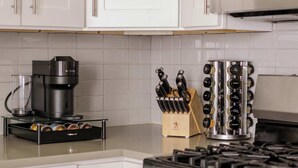 A kitchen with white cabinets, a coffee maker, a knife block, and a stove. - Designer Loft 4E | Heart of Gold Coast/River North (Chicago)