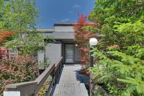 A wooden deck leading to a building with a grey exterior and a glass door. - Luxury Poconos Townhouse with Resort Perks! (Tannersville)