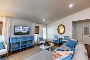 Un salon avec un téléviseur, des meubles bleus, un miroir et une porte.