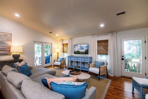 Uma sala de estar espaçosa com um sofá cinzento, almofadas azuis, uma mesa de centro e uma televisão fixada na parede.