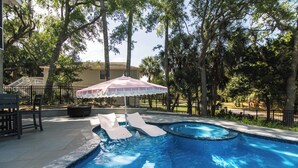 Una piscina con sillas de descanso y una sombrilla, rodeada de árboles y una cerca.