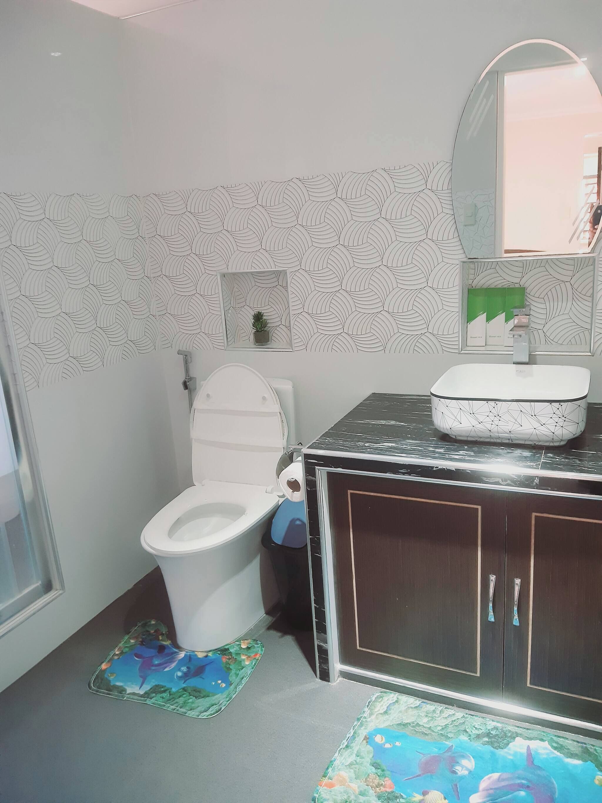 A bathroom with a toilet, a sink, a mirror, and a patterned wall.