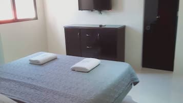 A bedroom with a bed, a flat-screen TV mounted on the wall, a dark-colored dresser, and a door.