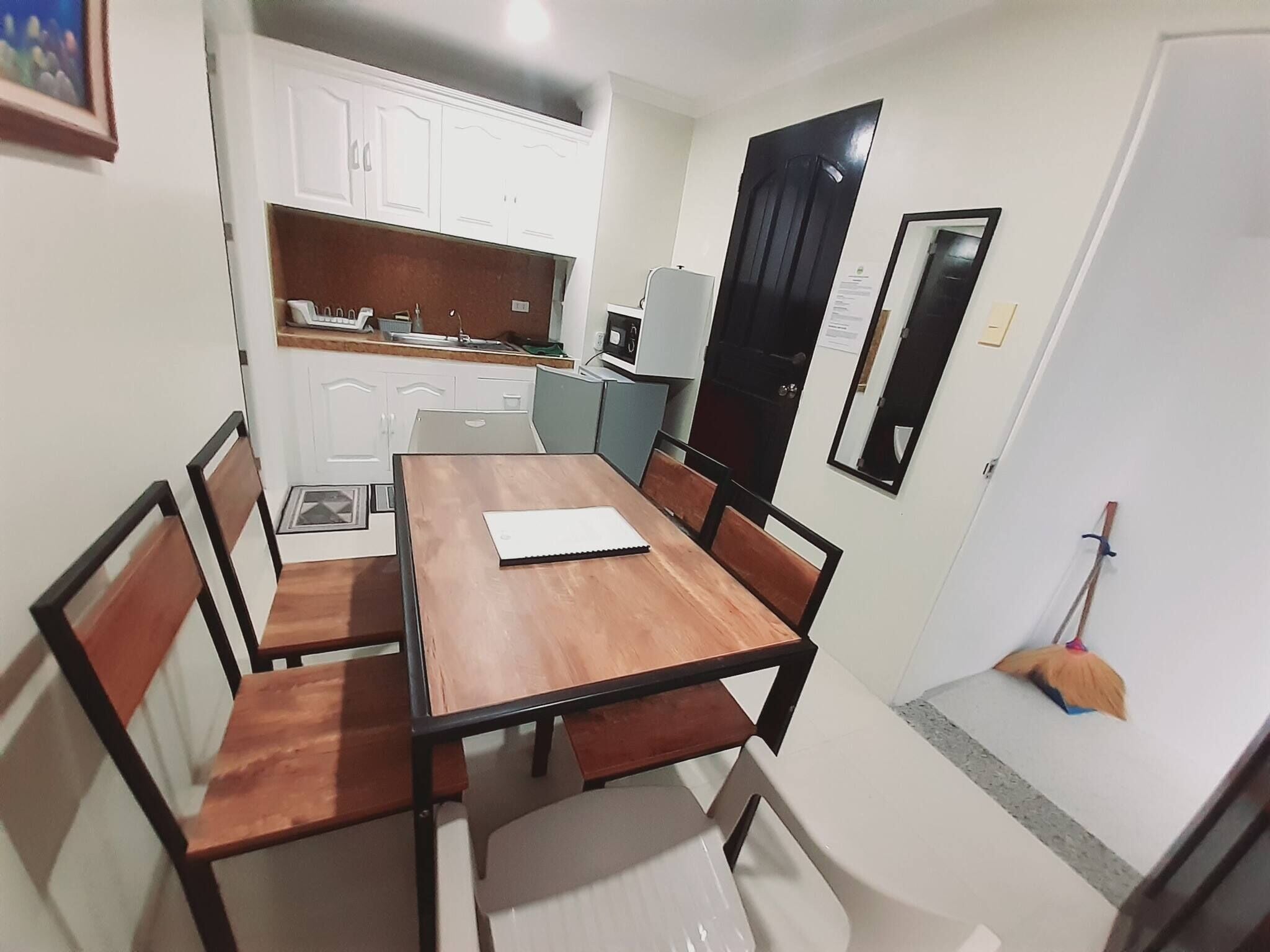 A compact dining area with a wooden table and chairs, a small kitchen with cabinets and appliances, and a broom leaning against the wall.