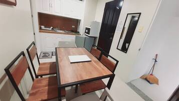 A compact dining area with a wooden table and chairs, a small kitchen with cabinets and appliances, and a broom leaning against the wall.