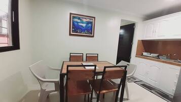 A dining area with a table and chairs, a kitchen with white cabinets, and a framed picture on the wall.