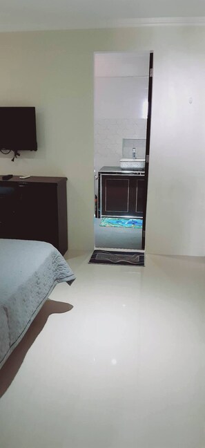 Un dormitorio con cama, cómoda, televisor y baño visible a través de una puerta abierta.