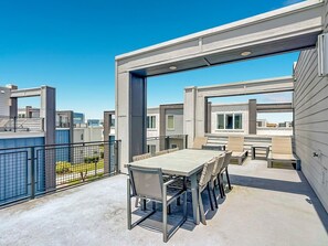 A rooftop patio with a table and chairs, a railing, and a view of other buildings. - Luxury 5BR Condo with Rooftop Terrace Near Disney (Kissimmee)