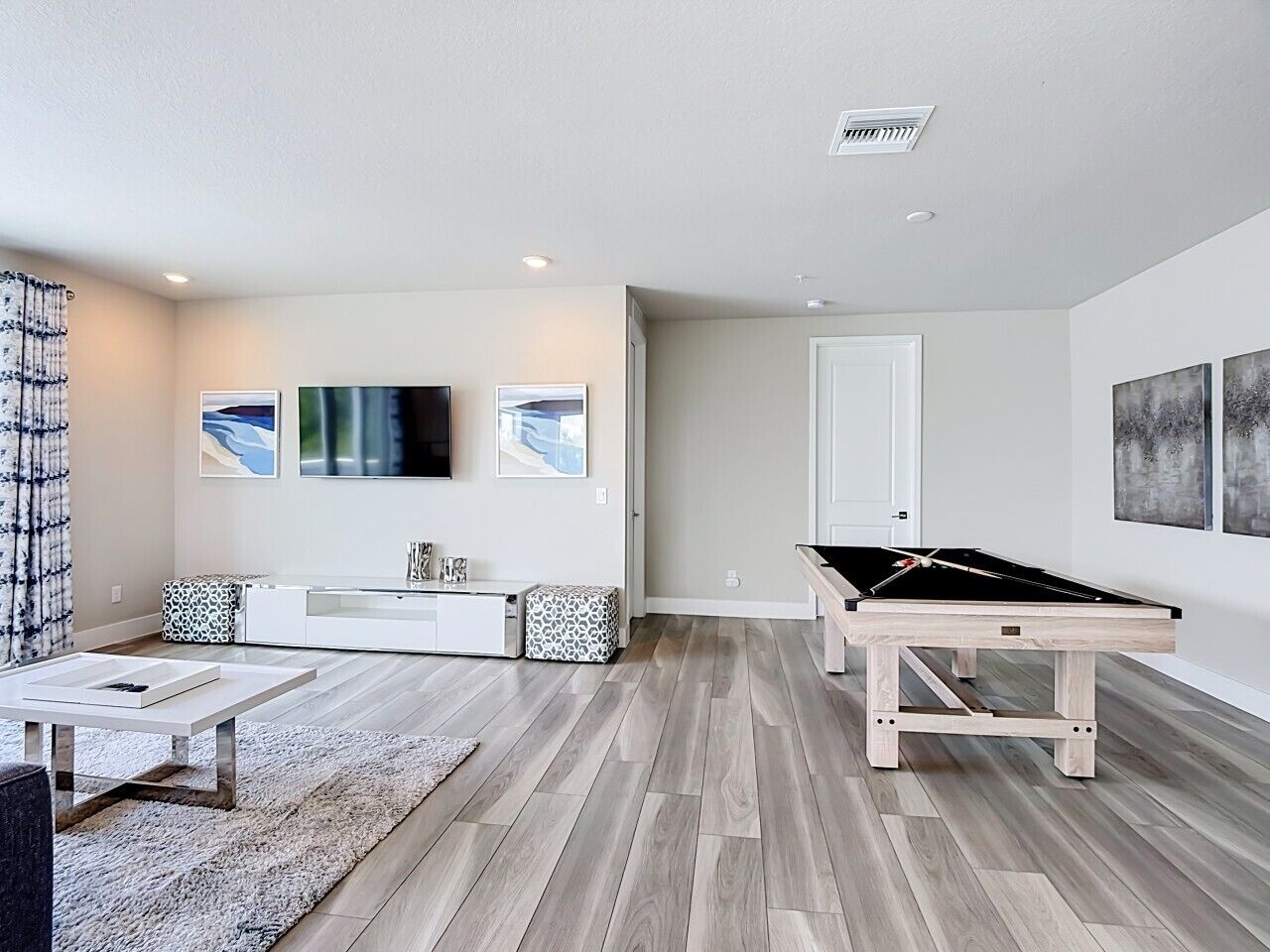 Un salon moderne avec une table de billard, un canapé, une table basse et des œuvres d’art accrochées aux murs.