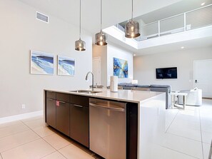 Een moderne keuken met een centraal eiland, roestvrijstalen apparatuur, hanglampen en kunstwerken aan de muren.