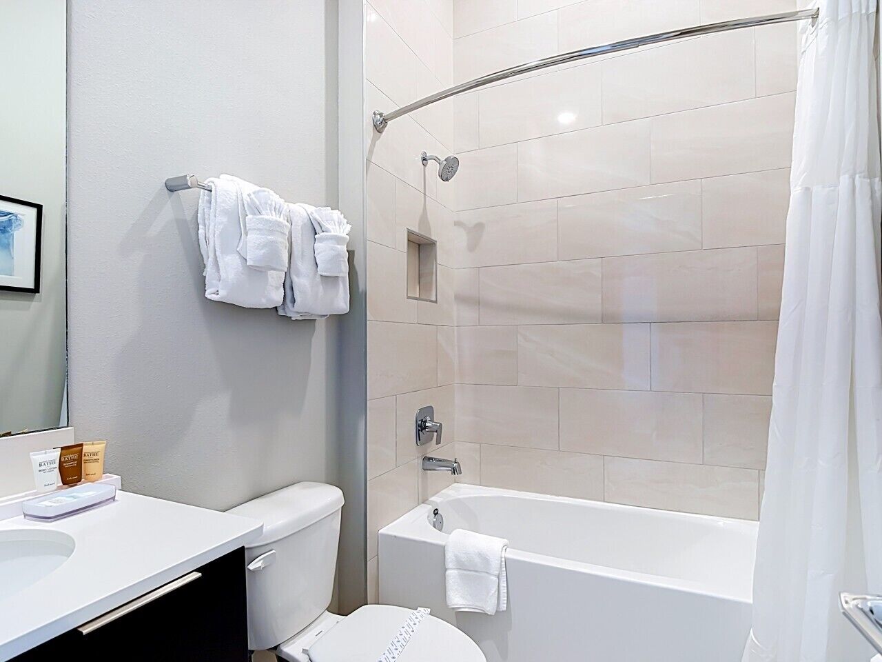 Un baño moderno con inodoro, lavamanos y bañera. Hay toallas colgadas en la pared y una cortina de ducha.