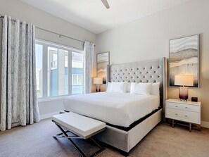 Een slaapkamer met een groot bed, nachtkastjes, een bankje en een raam met gordijnen.