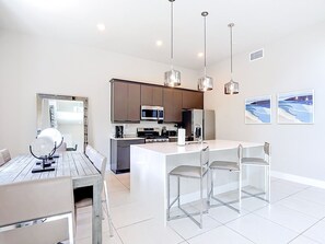 Uma cozinha moderna com eletrodomésticos de aço inoxidável, uma ilha central com banquetas e iluminação pendente.