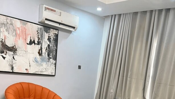 Ein modernes Wohnzimmer mit einer Couch, einem orangefarbenen Sessel, einem kleinen runden Tisch und einem großen abstrakten Gemälde an der Wand.