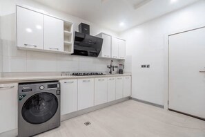 A modern kitchen with white cabinetry, a built-in washing machine, and a stove. - Radiant 1-Bedroom Apartment in Lekki 1 with Fast Wi-Fi & 24/7 Power (Lagos)