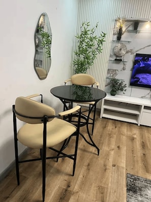 A dining area with a round table and four chairs, a mirror on the wall, and a television on a shelf. - Radiant 1-Bedroom Apartment in Lekki 1 with Fast Wi-Fi & 24/7 Power (Lagos)