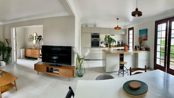 A modern kitchen with a central island, a dining area with a table, and a living space with a TV.