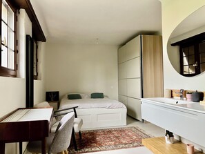 A bedroom with a bed, a desk, a chair, a wardrobe, and a bathroom with a mirror.