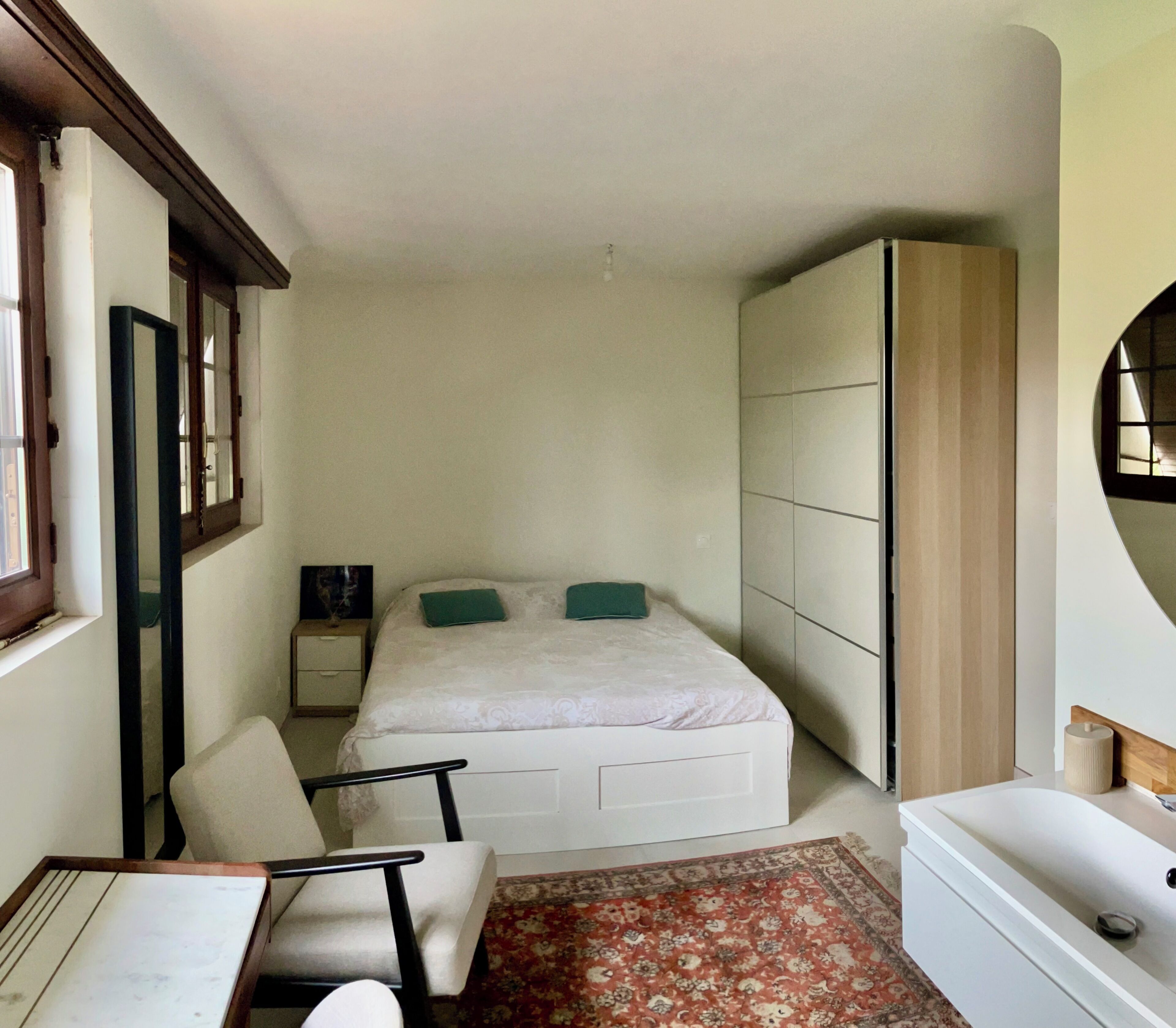Une chambre à coucher avec un lit, une chaise, une table de chevet, une armoire et une fenêtre.