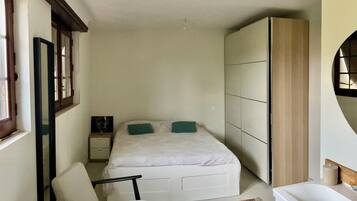 A bedroom with a bed, a chair, a nightstand, a wardrobe, and a window.