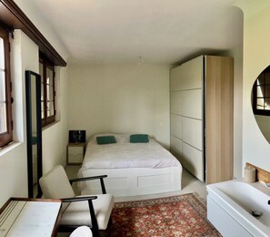 Un dormitorio con cama, una silla, una mesita de noche, un armario y una ventana.