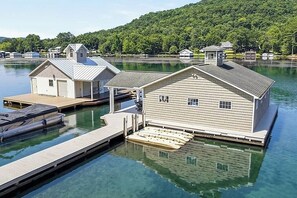 A waterfront property with docked boats, a wooden pier, and a house with a gabled roof. - Waters Edge- Lakefront Luxury on Lake Guntersville (Grant)