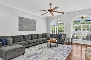 A living room with a sectional sofa, a coffee table, and a ceiling fan. - Waters Edge- Lakefront Luxury on Lake Guntersville (Grant)