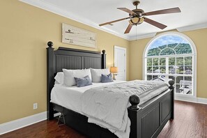 A bedroom with a bed, a ceiling fan, a window with a view, and a door. - Waters Edge- Lakefront Luxury on Lake Guntersville (Grant)