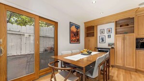 Un comedor con una mesa y sillas de madera, una ventana que da a una valla, y armarios de madera.