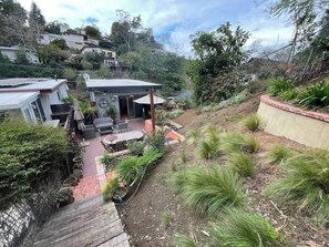 Ein Wohnhaus mit einer Terrassenfläche, Sitzgelegenheiten im Freien und einem Garten mit verschiedenen Pflanzen.