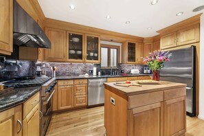 Eine moderne Küche mit Holzschränken, einem Edelstahlkühlschrank und einer zentralen Kochinsel mit Schneidebrett.