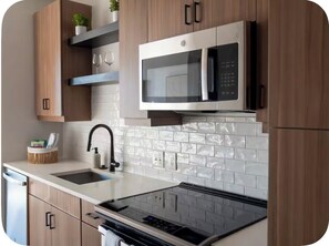 A modern kitchen with a built-in microwave, stainless steel appliances, and wooden cabinetry. - Modern Midtown Atlanta Retreat Near Mercedes-Benz Stadium (Atlanta)