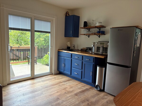 A kitchen with a sliding glass door leading to a deck, a Galanz refrigerator, and blue cabinets. - Fabulous modern bungalow with deck and private fenced yard. Dog friendly. (Crescent City)