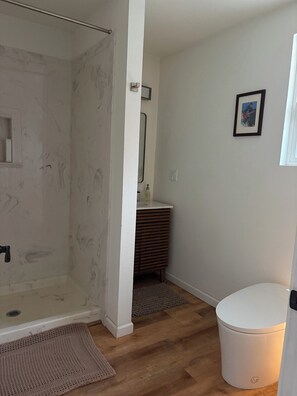 A bathroom with a shower, toilet, sink, and a framed picture on the wall. - Fabulous modern bungalow with deck and private fenced yard. Dog friendly. (Crescent City)