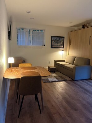 A compact living space with a dining table, chairs, a sofa, a cabinet, and a window with curtains. - Fabulous modern bungalow with deck and private fenced yard. Dog friendly. (Crescent City)