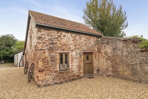 A rustic stone building with a tiled roof, a wooden door, and a window with a curtain. - 1 Bed Barn - Sleeps 2 - Pool - Garden - Bbq (Taunton)