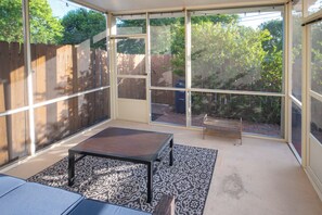 A sunroom with a bench and patterned rug, large windows, and a wooden fence outside. - Extended Stay in Townhome : Gated Community at Medical Center District (San Antonio)
