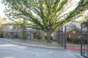 A residential area with brick houses, a metal fence, and a tree in the foreground. - Extended Stay in Townhome : Gated Community at Medical Center District (San Antonio)