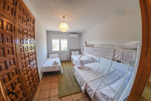 A compact hotel room with a wooden door, a single bed, a bunk bed, a window with blinds, and a hanging light fixture. - Casa Dolly - Elegant Villa directly on the Tajo (VIILLAMANRIQUE DE TAJO)