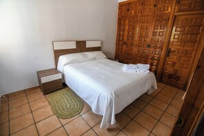 A bedroom with a bed, nightstand, woven rug, and wooden wardrobe. - Casa Dolly - Elegant Villa directly on the Tajo (VIILLAMANRIQUE DE TAJO)