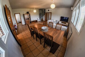 A dining area with a wooden table and chairs, a television, and a kitchen in the background.