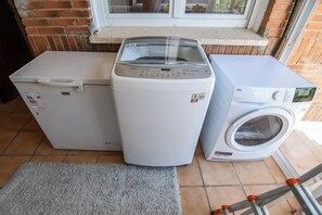 Two white washing machines and a dryer in a room with a tiled floor and a window above.
