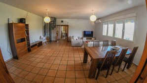 Un'ampia zona giorno con tavolo da pranzo, sedie, televisione e cucina sullo sfondo.